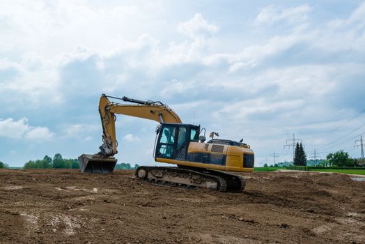 Big excavator parked on construction site with trees and cloudy blue sky in the background