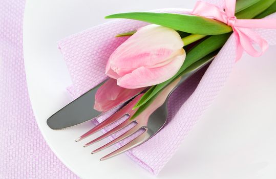 Romantic dinner / table setting with roses tulips and cutlery, on a white background. Copy space.