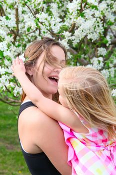 Little blond girld and her mom in a spring blossom garden