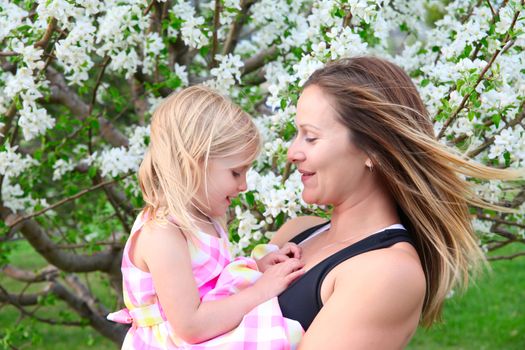 Little blond girld and her mom in a spring blossom garden