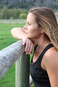 Beautiful female leaning against wooden fencing looking out