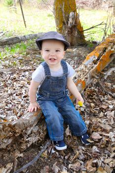 Little boy sitting outside in the field on a log