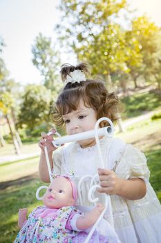 Adorable Young Baby Girl Playing with Her Baby Doll and Carriage Outdoors.