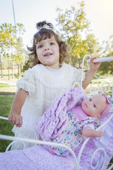 Adorable Young Baby Girl Playing with Her Baby Doll and Carriage Outdoors.