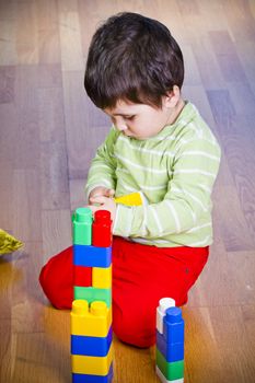 Brunette child playing with color tower toy in wooden room