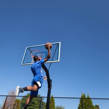 Young basketball player drives to the hoop for a high flying slam dunk.