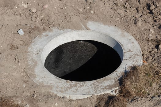 A round sewer hole with sand and rocks around it