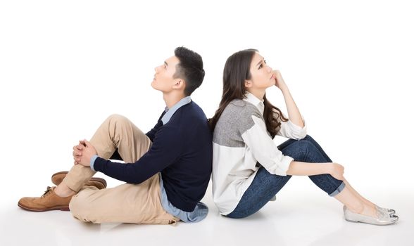 Young Asian couple sit on ground back to back and raise their head thinking on studio white background.