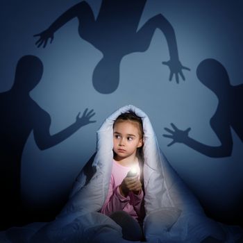 image of a girl under the covers with a flashlight the night afraid of ghosts