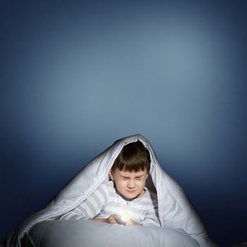 image of a frightened boy under the covers with a flashlight