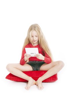 young girl on red pillow playing electronic game in studio against white background