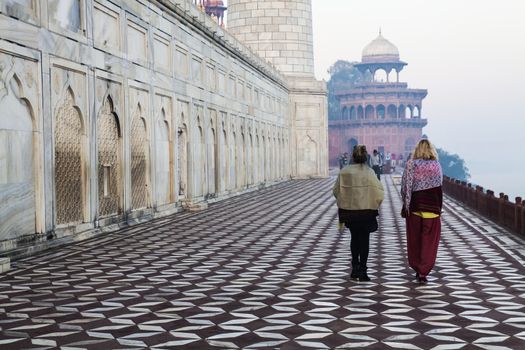 taj mahal is especially beautiful during winter mornings and i managed to get in very early to avoid the crowds. luckily i found this classical composition of leading lines of the brown and white patterned marble tiles on the floor with the marble trellissed base of taj and the railing on either side nicely pointing to  the two ladies enjoying the taj. the minaret in the background  completes the picture. the winter haze adds to the scene.