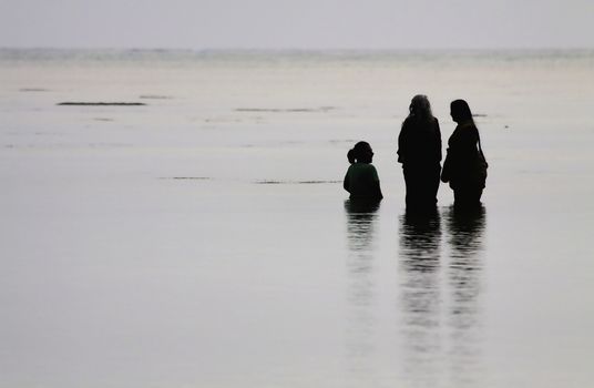 A Grandmother, her daughter and her Grand-daughter bathing at sea on a cloudy  morning in the calm waters of andaman sea at havelock island in the andamans, india make for an arresting picture.