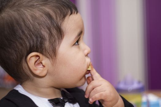 Adorable happy baby eating chocolate, wearing suit and bow tie