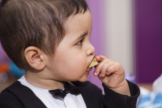 Adorable happy baby eating chocolate, wearing suit and bow tie