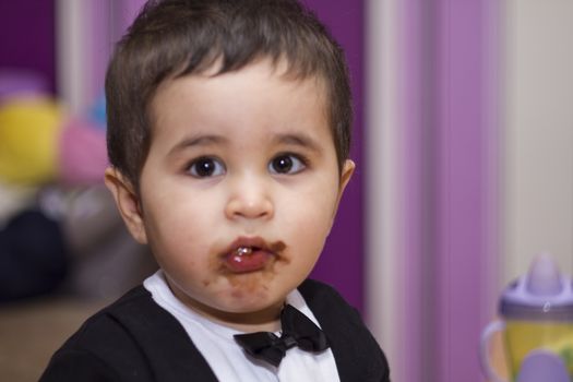 Sweet, Adorable happy baby eating chocolate, wearing suit and bow tie