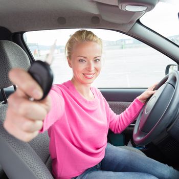 Woman driver showing car keys. Young female driving happy about her new car or drivers license. Caucasian model.