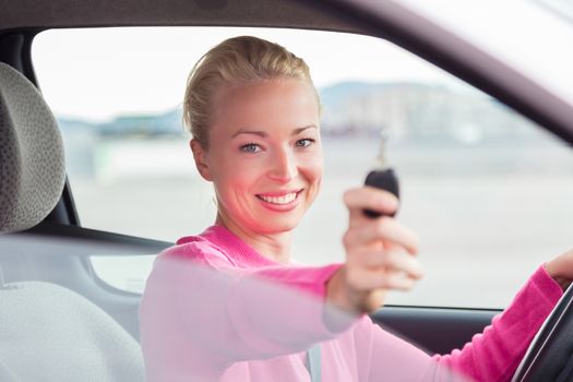 Woman driver showing car keys. Young female driving happy about her new car or drivers license. Caucasian model.