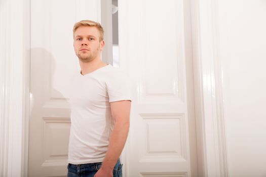 A young blonde man coming home passing through the door.