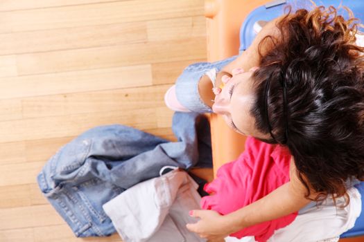 A young woman sitting on a stack of suitcases with too much clothes to fit in.