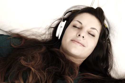 A young adult woman listening music with headphones in bed.