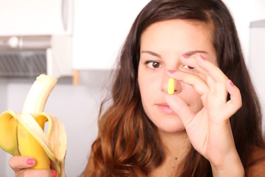 A young woman holding a supplement pill in one hand and a banana in the other.