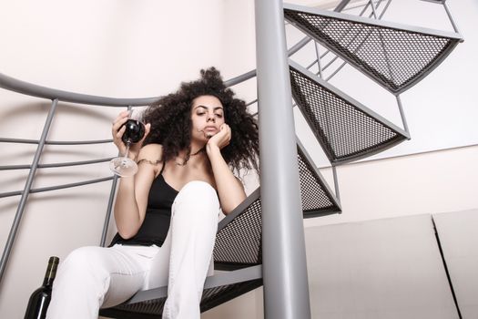 A young brazilian woman sitting on the stairs with a glass of red wine.