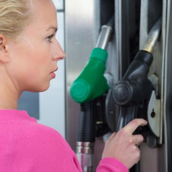 Woman pumping gasoline fuel in car at gas station. Petrol or gasoline being pumped into a motor vehicle car.