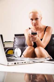 A blonde girl watching TV with the remote control in her hands
