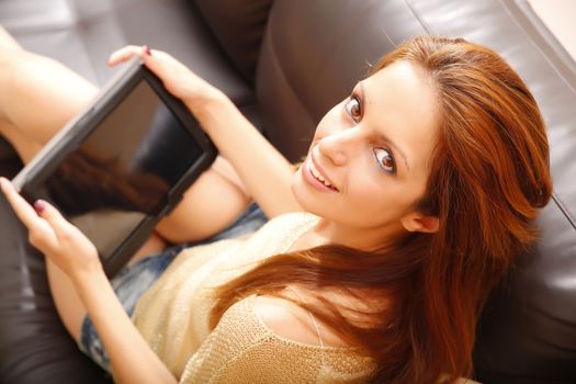 A young woman holding a Tablet PC while relaxing on the sofa.