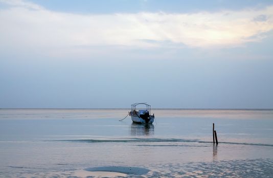 Single Boat seen anchored near shoreline on a calm sea in blue light of dawn