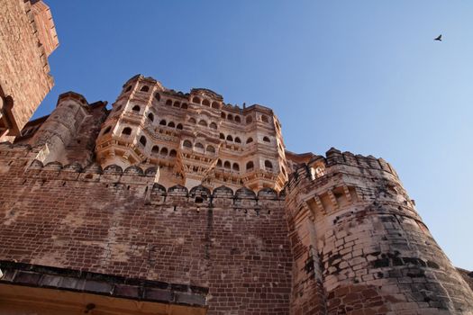 the meherangarh hill fort in jodhpur, rajasthan, india is a majestic fort soaring four hundred feet into the sky. immediately on entering through the main gate,  the imposing sight of the redstone construction with towers , peepholes and windows present an arresting sight for any visitor