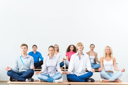 group of young people meditating in office at desk, group meditation