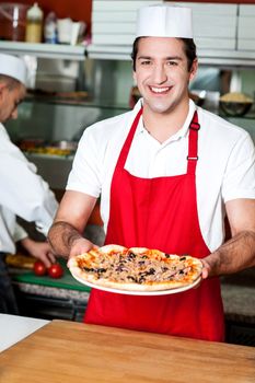 Smiling young male chef handing over pizza
