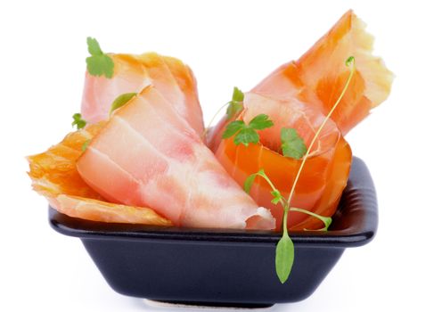 Snack of Swirled Slices of Delicious Smoked Sturgeon with Greens in Black Bowl isolated on white background