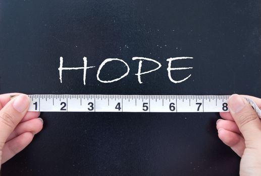 Tape measure held up against the word hope handwritten on a chalkboard