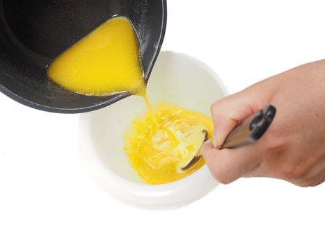 Person adding melted butter from kettle into blend in plastic bowl whilst stirring