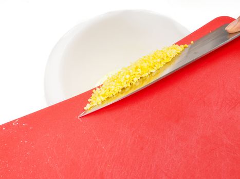 Someone adding chopped lemon zest from a red cutting board with the side of a knife towards white