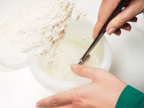 Female person mixing flour into the melted blend of butter and egg yolk with a black spatula