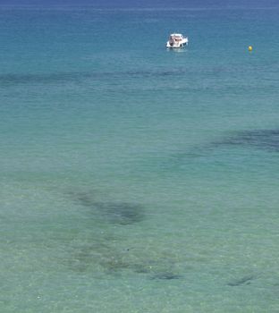 Azure Mediterranean background white boat with unrecognizable people and yellow buoy shallow warm inviting water in the foreground.