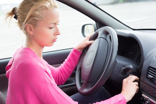 Beautiful casually dressed female car driver starting the engine.