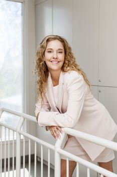 Smiling proud business woman standing in office hallway leaning on railing