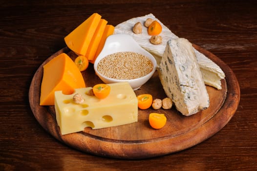 various cheeses with nuts and fruits on wooden plate