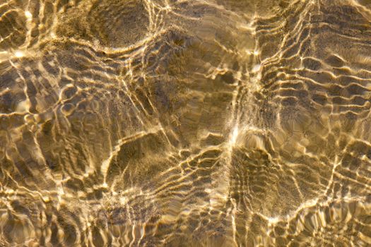 Sunny shallow water ripples over yellow sand bottom