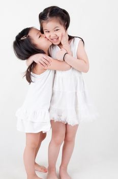 Little girls portrait. Asian sisters kissing on plain background. Sibling love.