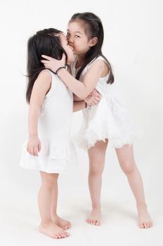 Little girls portrait. Asian sister kissing sibling on plain background.