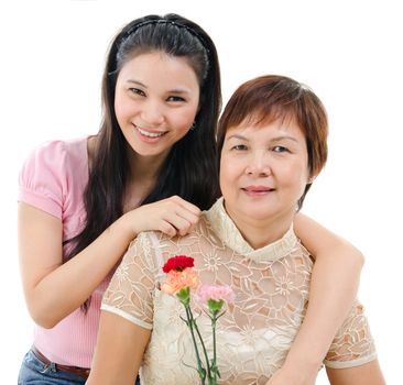 Senior mother holding carnation flower, adult daughter embraces mom, isolated on white background. Mixed race Asian family portrait. 