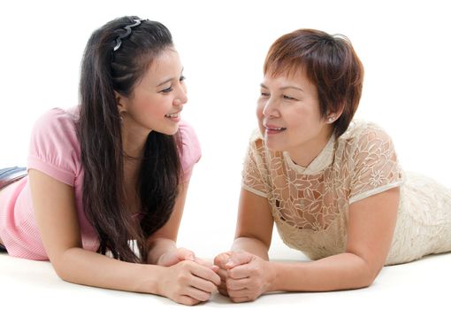 Senior mother and adult daughter lying on floor and chatting, isolated on white background. Mixed race Asian family portrait. 