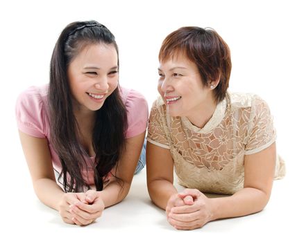 Senior mother and adult daughter lying on floor, having joyful conversation, isolated on white background. Mixed race Asian family portrait. 