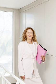 Happy confident business woman standing in office hallway holding binder